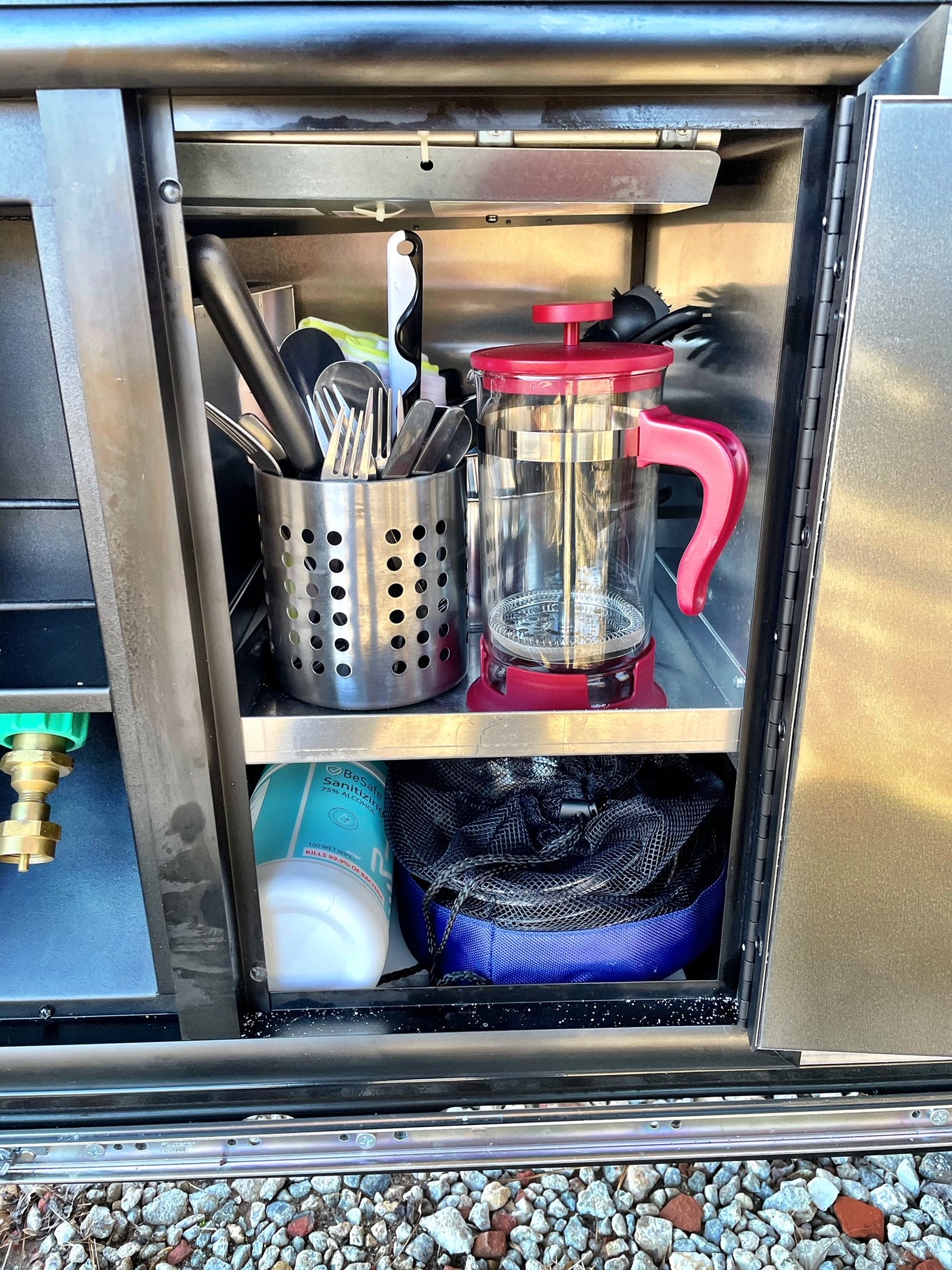 RV rental: stainless steel compartment organized with utensils, red French press, & sanitizing wipes.