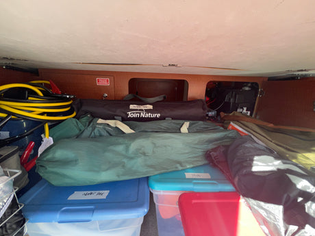 RV rental storage space packed with camping gear like a portable table, hoses, and organized bins.