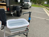 RV rental outdoor kitchen: Portable wash basin with faucet on a table, ready for use beside a camper trailer.