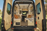 Cozy custom rv rental camper van interior with open rear doors, featuring bench seating, wood paneling, and a compact living space.