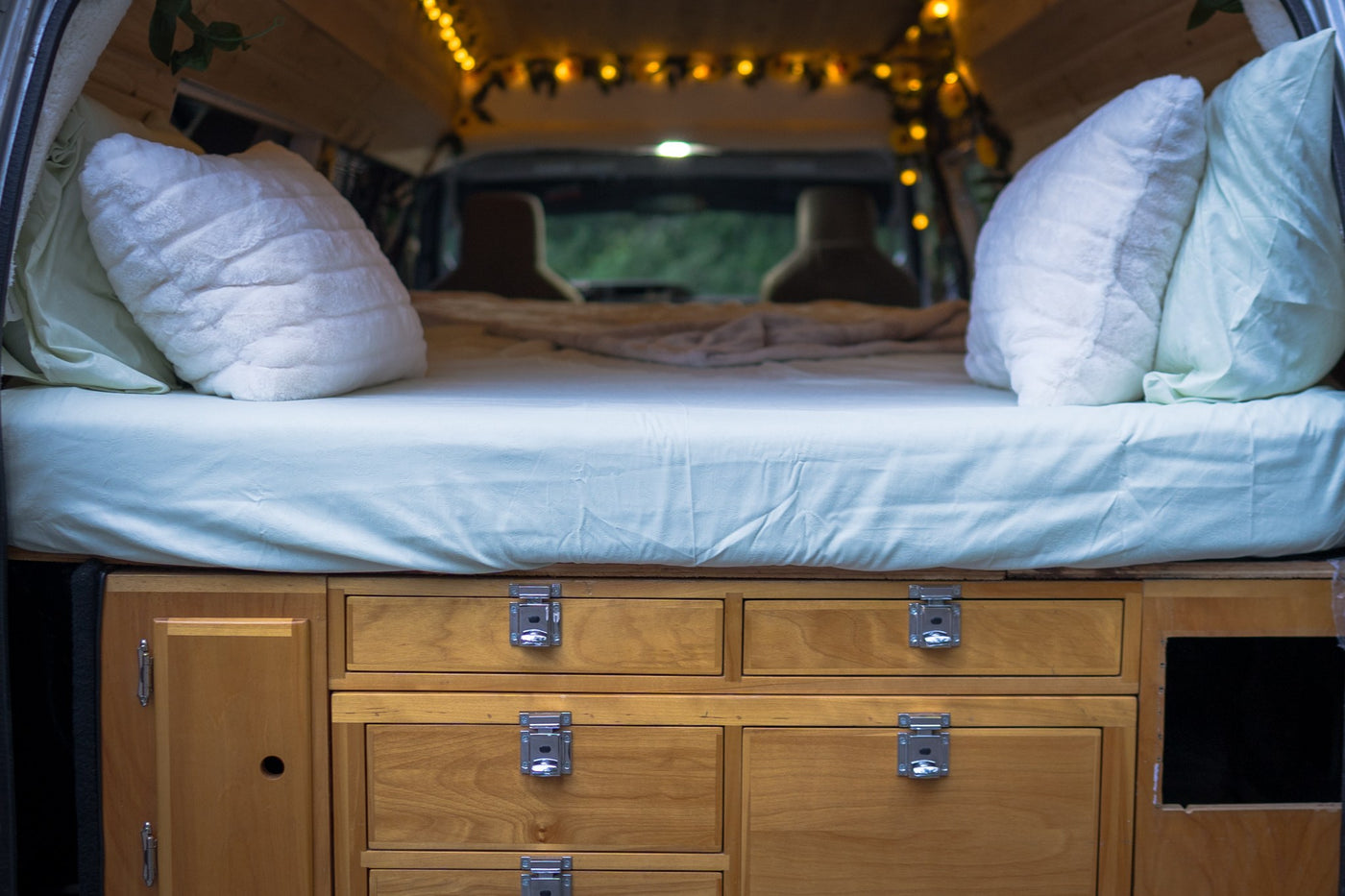  and a cheerful sunflower "WELCOME" sign by the window.|Cozy RV rental interior: wood-paneled ceiling with warm string lights and decorative foliage. Front seats visible — photo 2