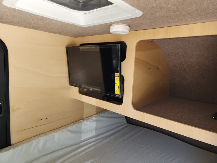 RV rental interior showing a comfortable bed, wall-mounted TV, and storage cubby. Perfect for road trips!