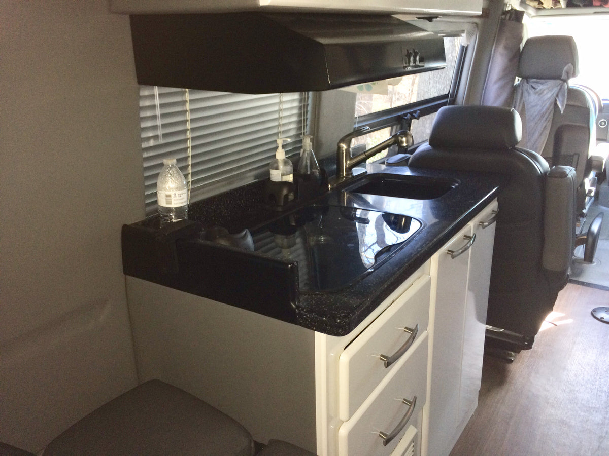 Experience comfort in this RV rental: Features a well-equipped kitchen with sink, dark counters, and plush front seats. — photo 6