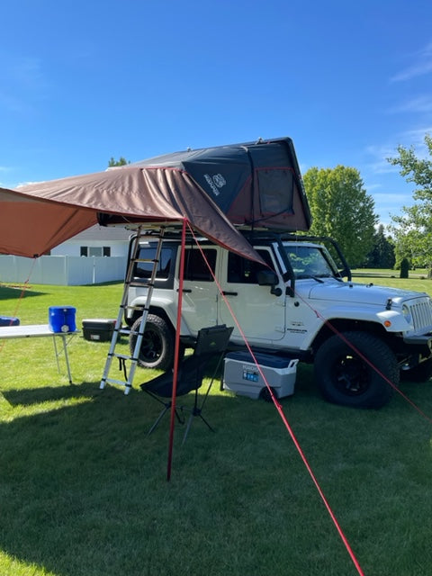 White Jeep with rooftop tent & awning deployed for overland camping. A unique RV rental alternative for adventures.