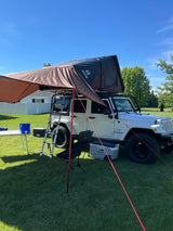 White Jeep with rooftop tent & awning deployed for overland camping. A unique RV rental alternative for adventures.