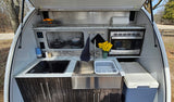 Compact outdoor RV rental kitchen with Dometic stovetop, sink, microwave, and cooler for convenient camping.