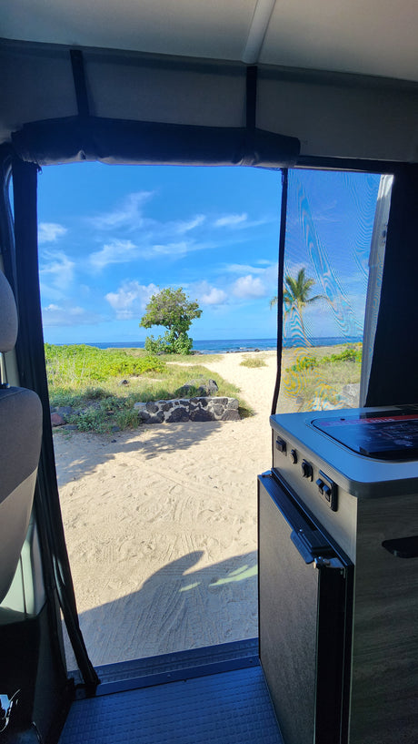 Inside a comfortable rv rental, gaze at the serene beach. View through the large window shows sand, ocean, and sky.