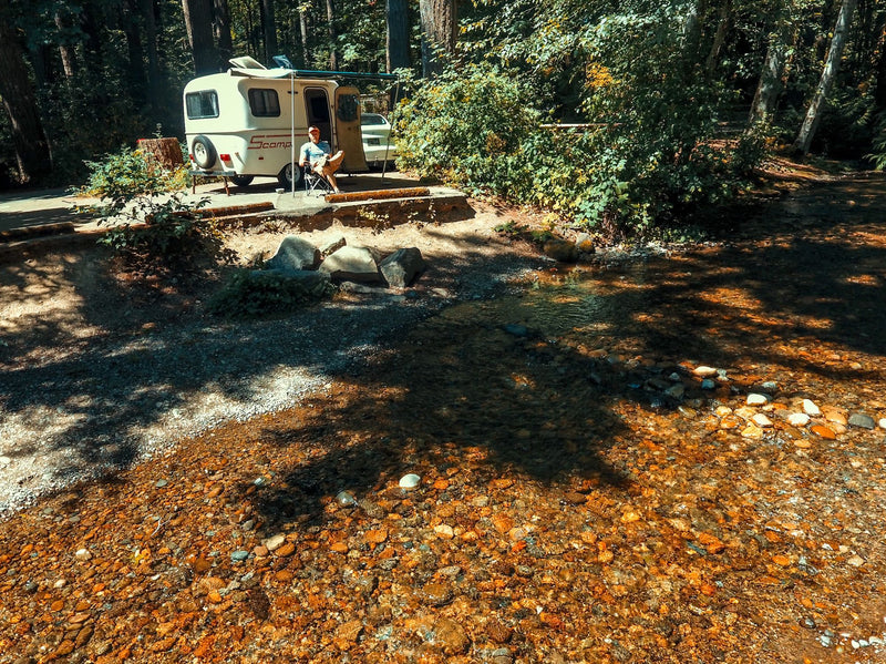 Man relaxing by a clear forest creek with his RV rental at a serene campsite. — photo 15