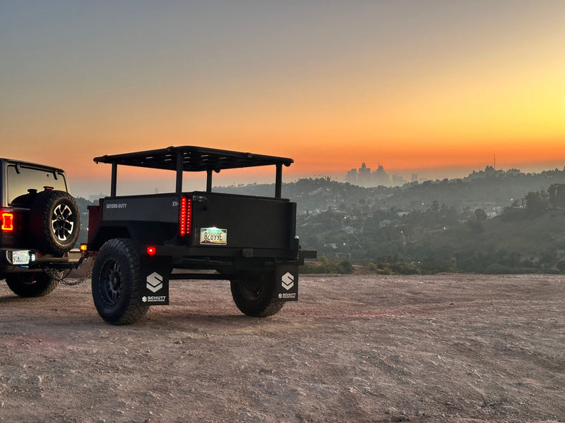 A dark Jeep tows a rugged Schutt Industries overland trailer at sunset, overlooking a hazy city. Ideal for your next RV rental adventure. — photo 10