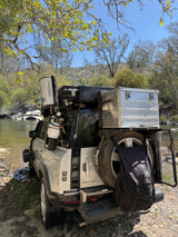 Outfitted Land Rover Defender for RV rental overlanding, parked by a river. Perfect for off-grid adventure camping.