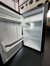Open compact refrigerator in an RV rental, showing interior shelves, a small freezer, and door storage. Ready for your trip!