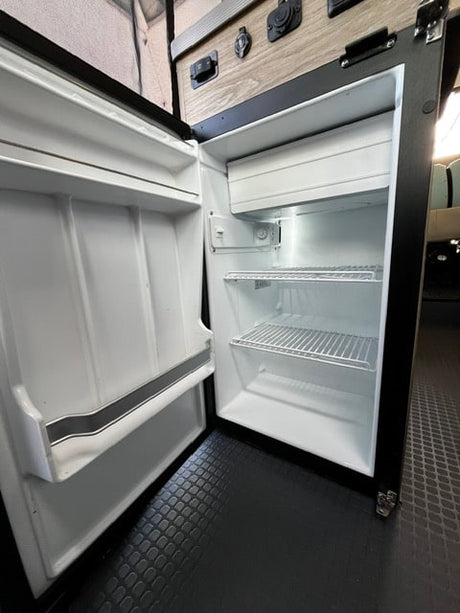 Open compact refrigerator in an RV rental, showing interior shelves, a small freezer, and door storage. Ready for your trip!