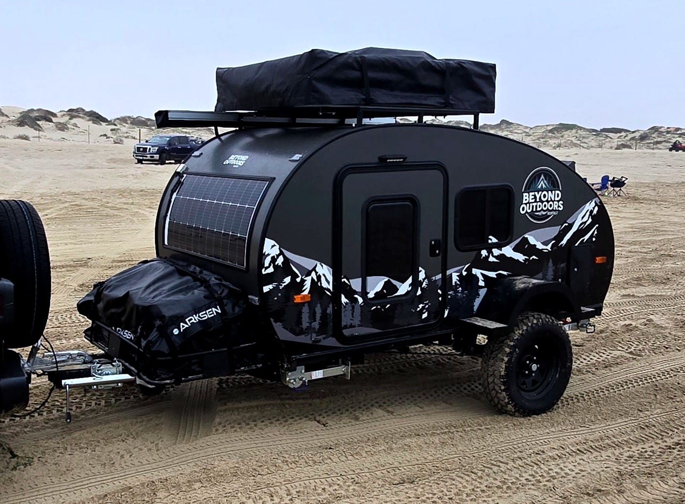 This Beyond Outdoors off-road teardrop camper, ideal for rv rental, features solar panels and rooftop storage, parked on sandy dunes.