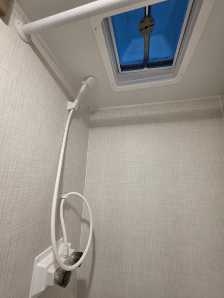Inside an RV rental: a compact bathroom with a white shower head, water controls, and a blue-tinted ceiling skylight.