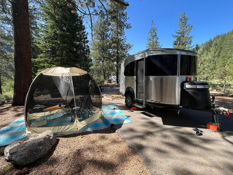 Perfect RV rental getaway! Airstream travel trailer with screen room set up at a peaceful forest campsite.|Enjoying an RV rental setup: A silver camper with awning — photo 1
