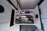 Compact RV rental kitchen drawer with neatly organized utensils: knives, forks, spoons, can opener, and spatulas.