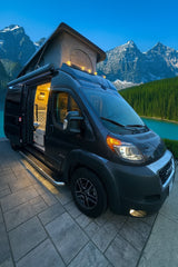 Explore nature's beauty in this RV rental camper van with pop-top roof. Illuminated interior at a stunning mountain lake.