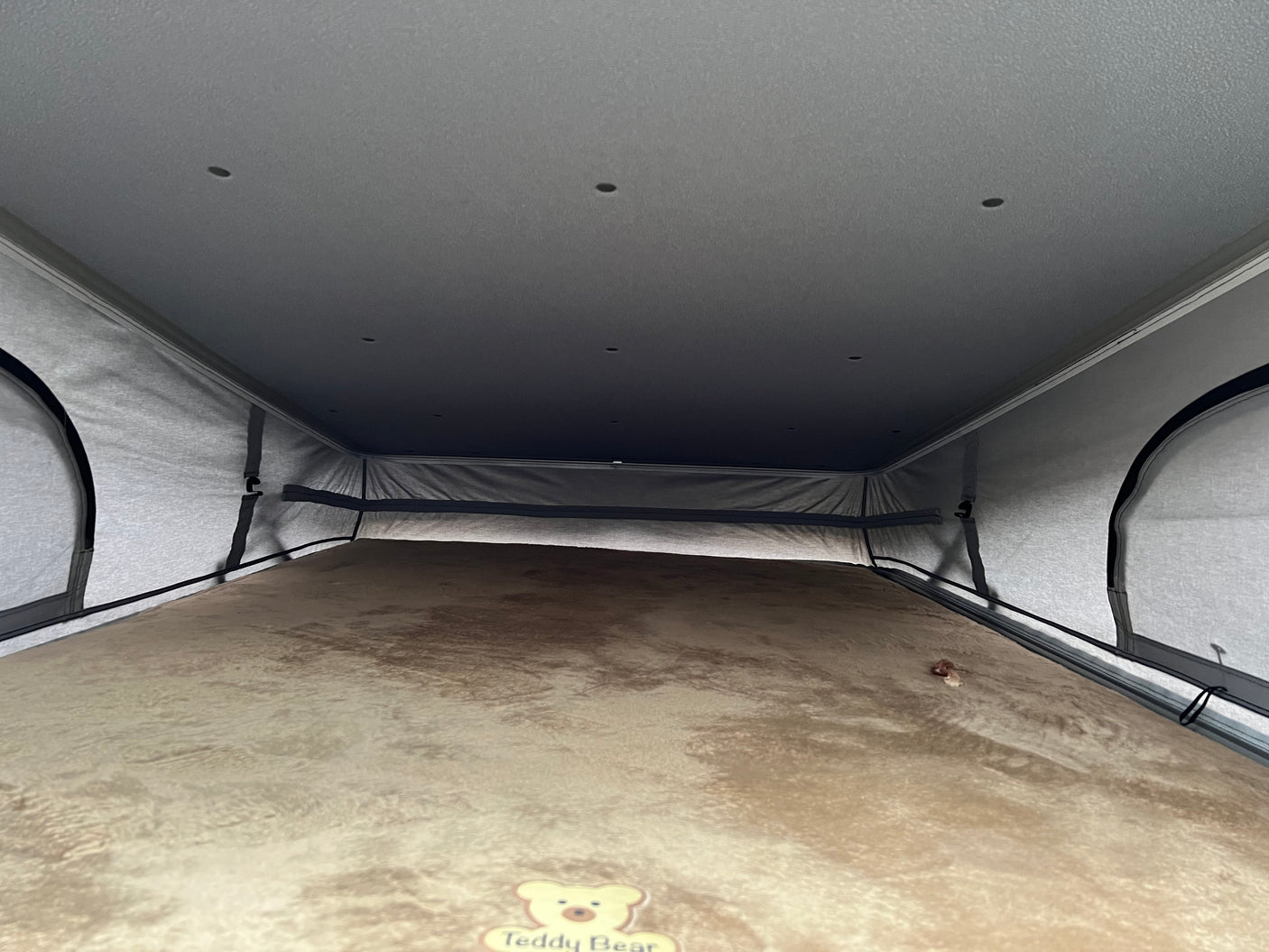 View inside an RV rental's pop-top sleeping area, featuring a soft, brown mattress and integrated ceiling lights.