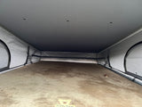 View inside an RV rental's pop-top sleeping area, featuring a soft, brown mattress and integrated ceiling lights.