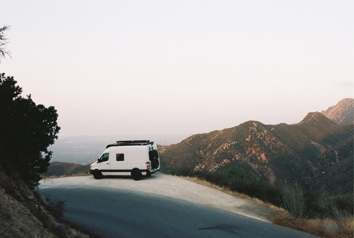 White camper van (RV rental) parked on a mountain overlook, offering stunning views of valleys and distant peaks. Ideal road trip!