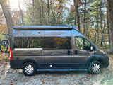 Explore nature with this grey Ram ProMaster camper van rv rental, featuring a bike rack, parked among sunlit trees.