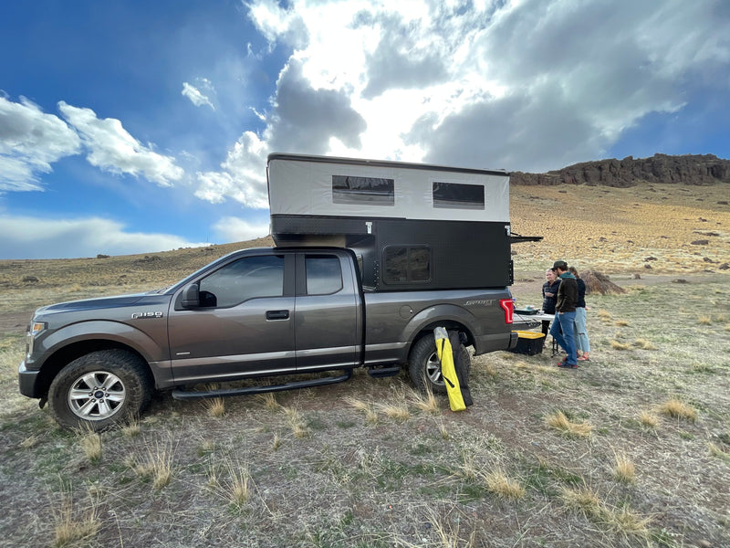 Grey Ford F-150 truck with a deployed pop-up RV rental camper. People gather by the back, camping in a desert. — photo 9