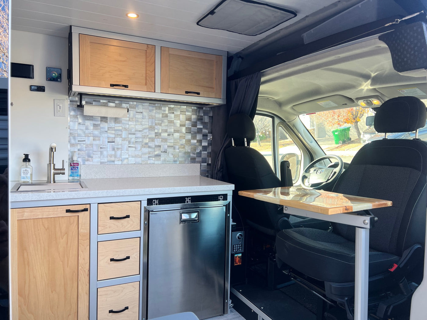 RV rental with a modern camper van kitchen: wood cabinets, tiled backsplash, fridge, sink, and swivel table. — photo 7