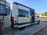 Explore with this white Sprinter camper van, an ideal RV rental. Side door open, it features a rear ladder & roof awning for adventure.