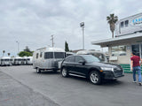 An Audi SUV is hitched to a silver Airstream travel trailer at an RV rental lot with more Airstreams visible.