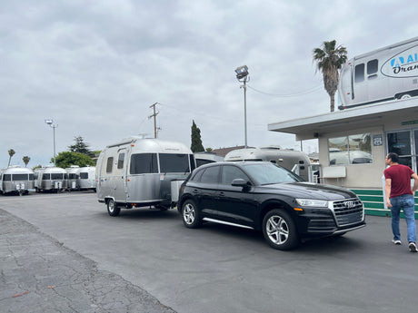 An Audi SUV is hitched to a silver Airstream travel trailer at an RV rental lot with more Airstreams visible.