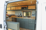 Inside a modern **RV rental** van: bed, kitchenette, wood ceiling, and ample storage for mobile living.