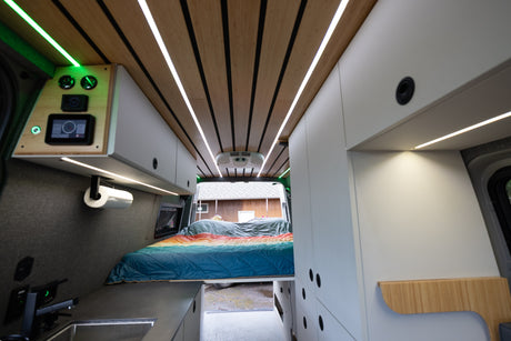 Explore this modern rv rental camper van interior: sleek wood ceiling, tech controls, compact kitchen, and cozy bed.