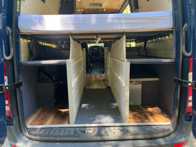 Explore this RV rental's versatile camper van interior, featuring a raised bed, two lower bunks, and organized storage spaces.