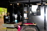 This RV rental features a well-equipped outdoor camp kitchen. Visible are a stove, utensils, spices, and a small prep area, ready for cooking.
