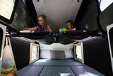 RV rental fun! Two girls enjoy the upper bunk of a family-friendly camper interior. Lower bed and window visible.