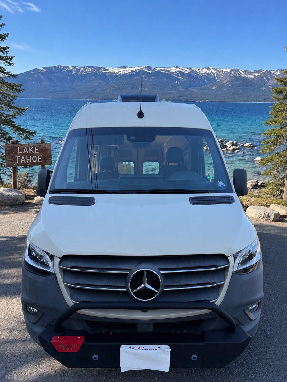  and bench seating.|Enjoy an rv rental! Rear view of a white Mercedes Sprinter van overlooking a clear blue lake framed by pine trees and distant mountains.|This rv rental van's front cabin features black driver and passenger swivel seats — photo 2