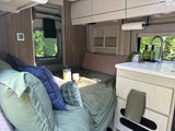 Enjoy this inviting RV rental interior, featuring a cozy bed, compact kitchen, and travel essentials like coffee.