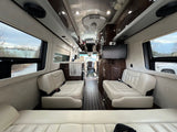Spacious luxury RV rental interior features cream leather seating, rich wood, TV, and large windows for scenic rides.