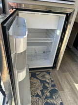 Inside an RV rental: a clean, empty compact refrigerator, featuring shelves, door bins, and an interior light.