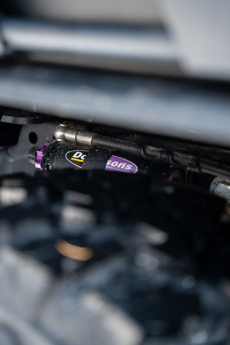 Close-up of a dusty Dobinsons suspension shock with purple accents, enhancing your RV rental's off-road capability.