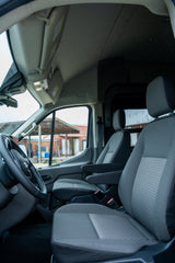 Inside an RV rental van. View from rear shows driver's cabin, comfy front seats, & outdoor scene through windshield.