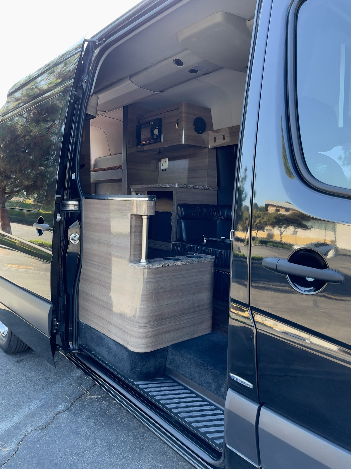 Open side door of a sleek black RV rental van, revealing a custom interior with compact kitchen and lounge area. — photo 9