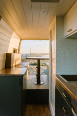 Experience stunning views from your RV rental! Cozy van interior with kitchen & dining, looking out to ocean.