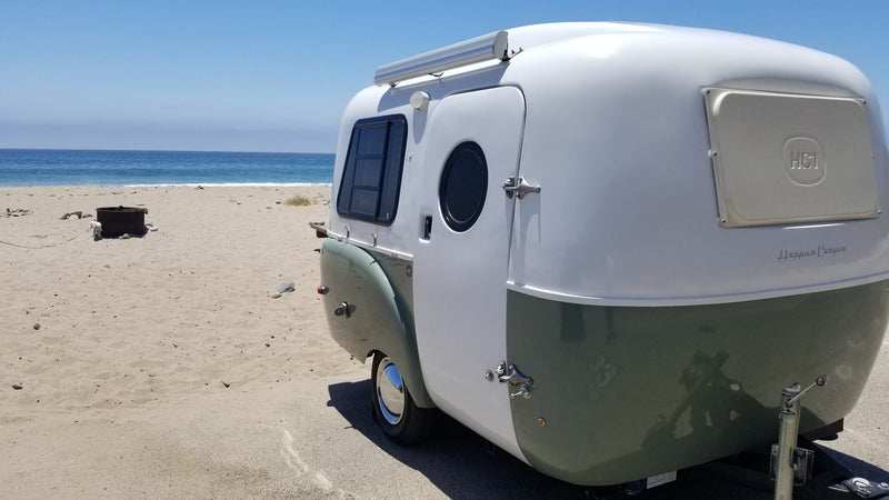 A stylish, two-tone Happier Camper at a serene beach. This RV rental offers scenic ocean travel for outdoor enthusiasts. — photo 15