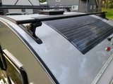 Top-down view of an RV rental roof with a flexible solar panel, roof rack, and a black hatch, for off-grid power.