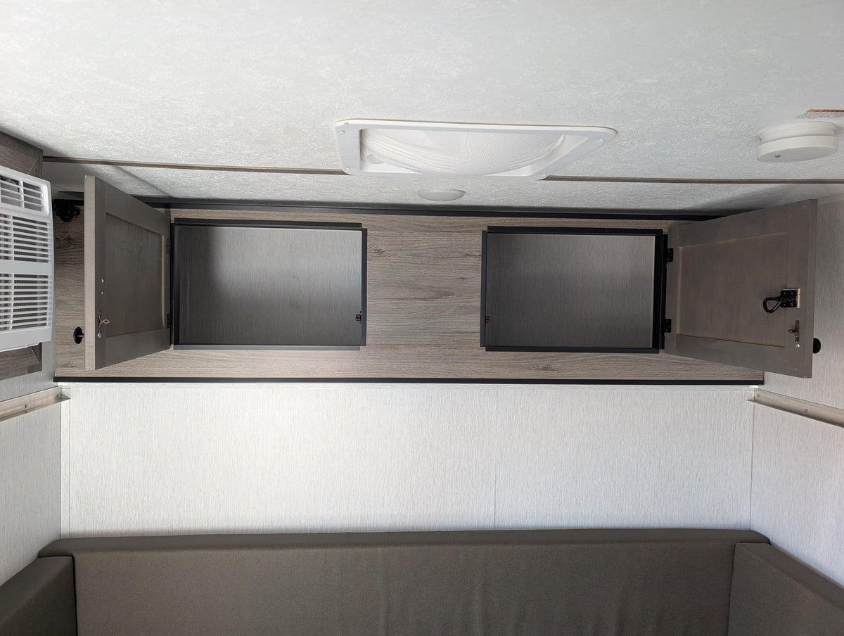 Modern rv rental interior: cozy bunk/sofa, open overhead cabinets, AC unit, and ceiling with light/detector. — photo 12