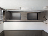Modern rv rental interior: cozy bunk/sofa, open overhead cabinets, AC unit, and ceiling with light/detector.