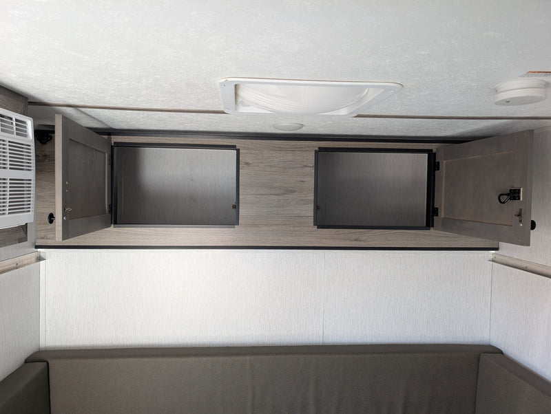 Modern rv rental interior: cozy bunk/sofa, open overhead cabinets, AC unit, and ceiling with light/detector. — photo 12