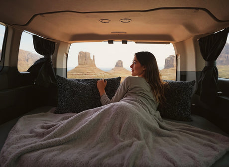 Cozy rv rental setup: A woman relaxes in bed, admiring Monument Valley's desert formations. Perfect for van life adventures!