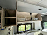 Inside an RV rental: open overhead cabinets with clear bins, shelves, a window, and a bed. Functional space.